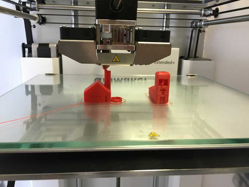 3D printer printing a red plastic house and building